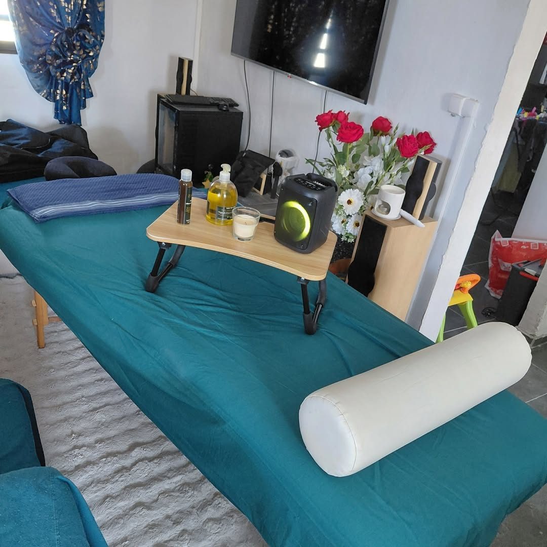 Table de massage installée dans un salon, avec huiles, bougie et roses